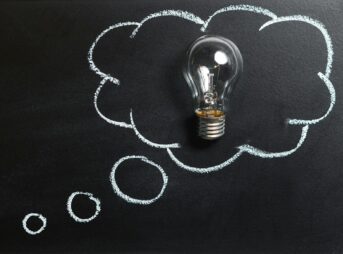 Light bulb laying on chalkboard with drawn thought bubble, symbolizing creative ideas.
